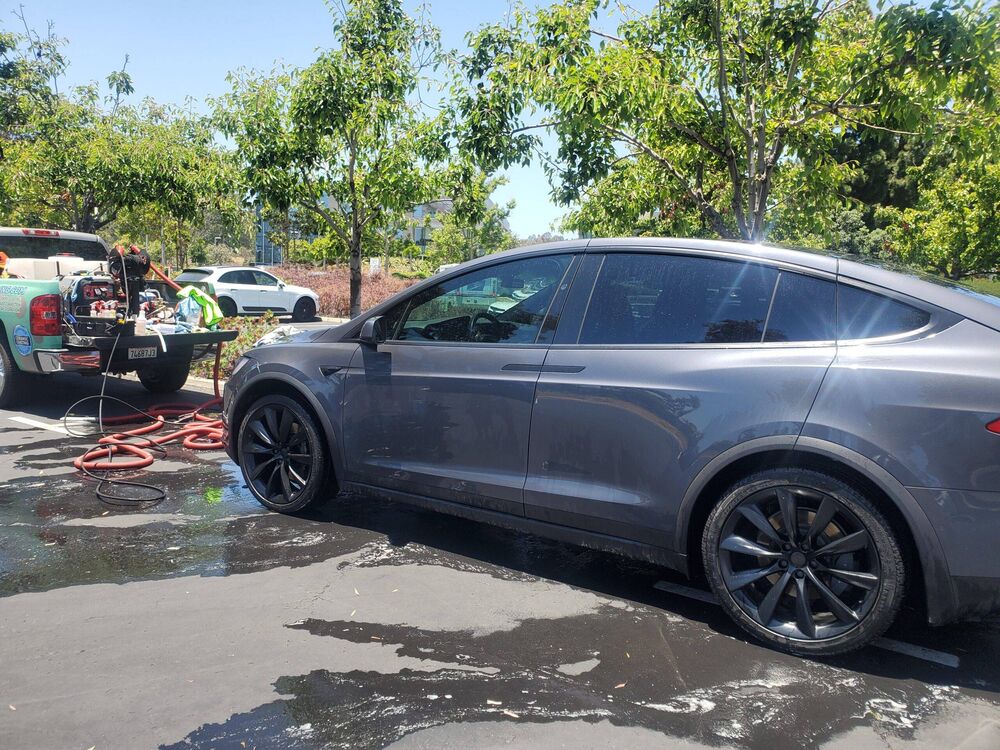 Gray Tesla Model Y being washed with a hose and detailing equipment nearby