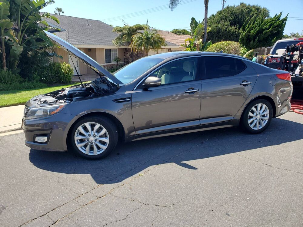 Silver Kia Optima sedan with the hood open during a detailing service