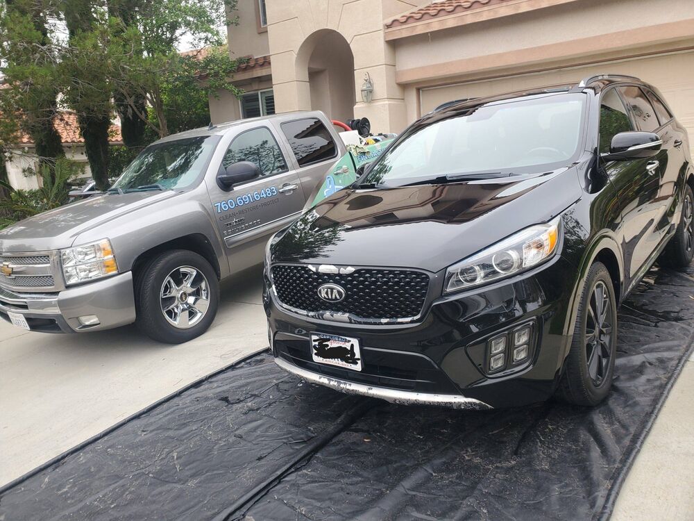 Black Kia Sorento SUV detailed in a driveway next to a work truck