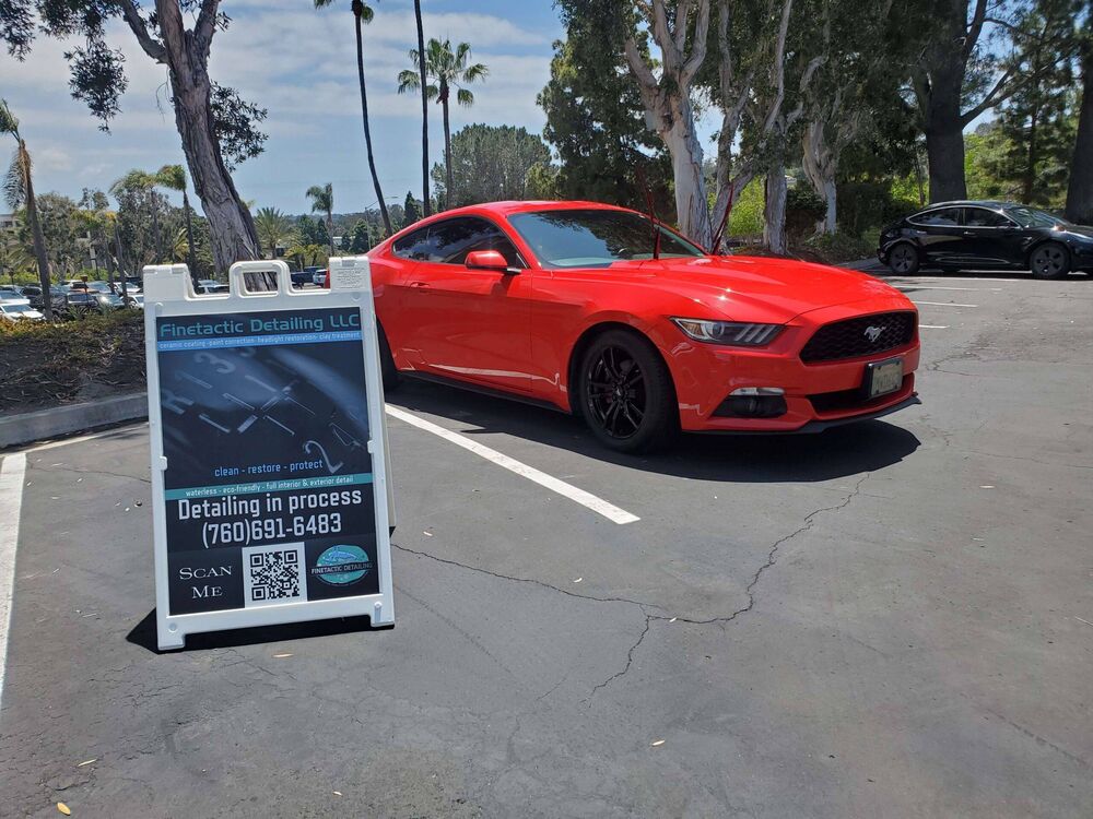 Red Ford Mustang detailed in a parking lot next to a Finetactic Detailing sign