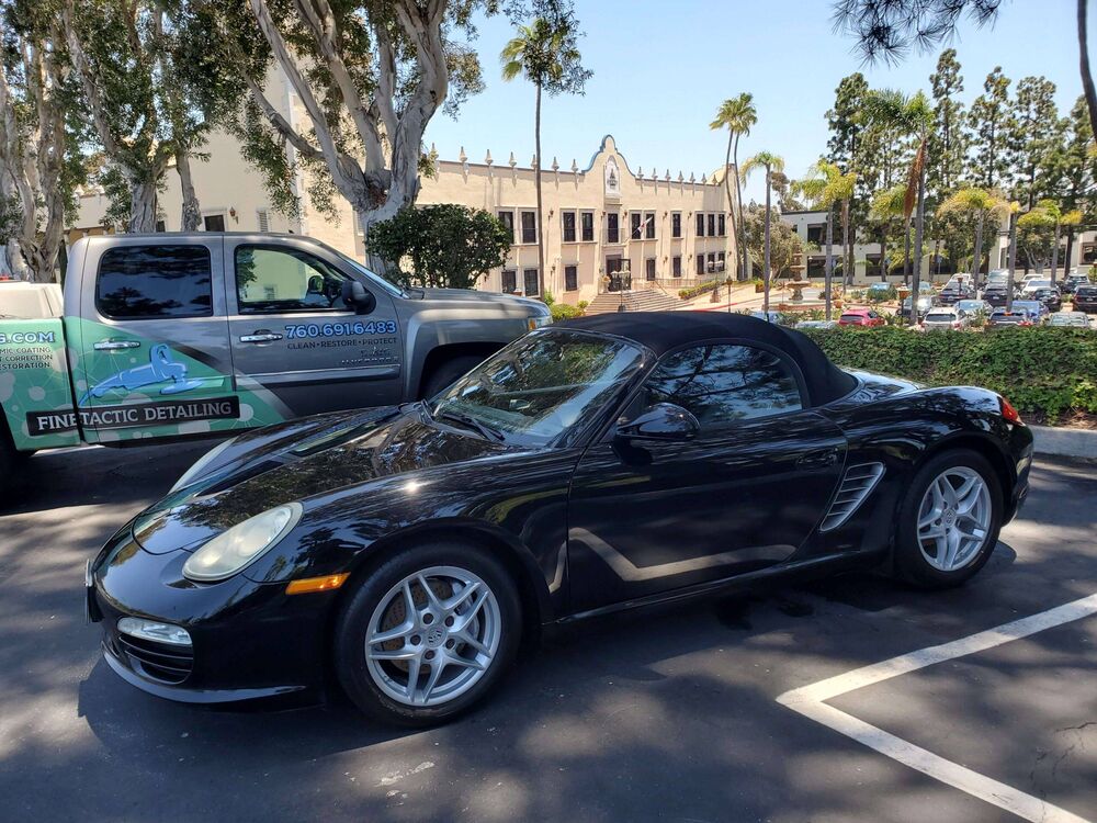 Black Porsche Boxster convertible parked after detailing, with the Finetactic Detailing truck in the background