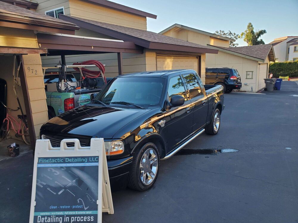 Black pickup truck detailed next to a Finetactic Detailing sign reading Detailing in process