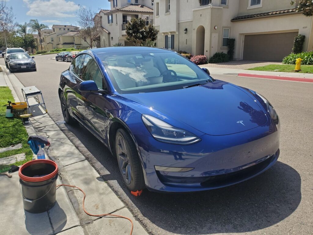 Blue Tesla Model 3 being washed with ceramic coating supplies