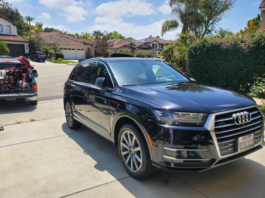 Black Audi Q7 detailed and shining in a driveway, with the mobile detailing truck parked nearby
