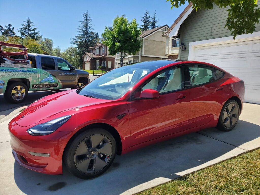Red Tesla Model 3 freshly detailed, with the Finetactic Detailing truck parked behind it